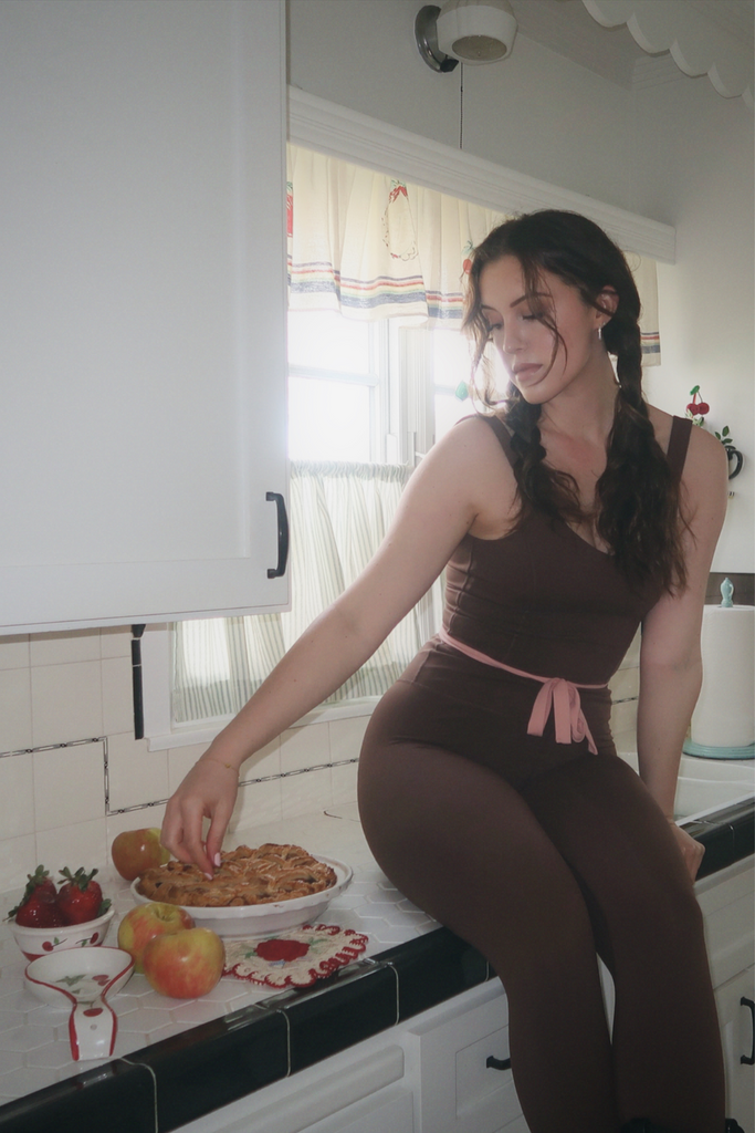 model sitting on kitchen counter wearing Fawn Jumpsuit while reaching for apple pie